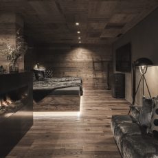 Camera da letto principale con caminetto e design raffinato nell'Chalet Seceda di Cortina Hospitality, finestre che offrono una vista incantevole del bosco.