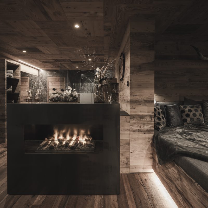 Camera da letto con caminetto nell'Chalet Seceda di Cortina Hospitality, un rifugio di lusso e calore per un sonno ristoratore.