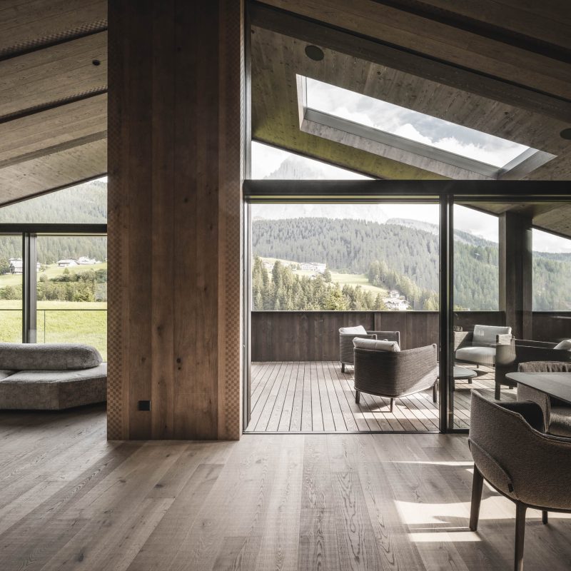 Grande salone minimalista con vista panoramica all'Chalet Gardena di Cortina Hospitality, evidenziando l'eleganza del design e l'abbondanza di luce naturale.