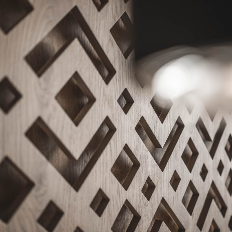 Closeup della parete in legno intarsiato presso l'Chalet Gardena di Cortina Hospitality, evidenziando l'artigianato raffinato e l'estetica unica.