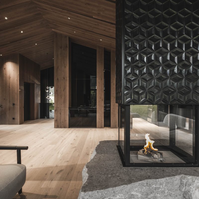 Caminetto a 360 gradi acceso nel living all'Chalet Gardena di Cortina Hospitality, regalando una vista incantevole e un'atmosfera magica.