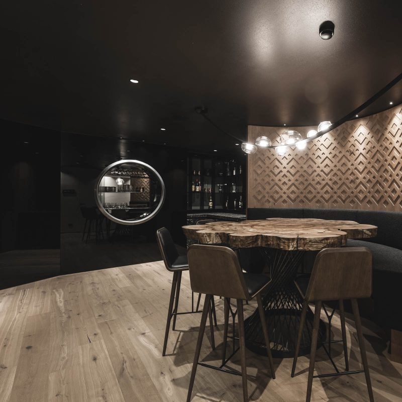 Stanza Leisure con tavolo in legno massiccio e angolo bar all'Chalet Gardena di Cortina Hospitality, rappresentando l'armonia tra la natura e il design sofisticato.