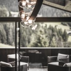 Lampadario di design e salottino sulla terrazza panoramica nella sala living all'Chalet Gardena di Cortina Hospitality, esprimendo un equilibrio sofisticato e lusso impeccabile