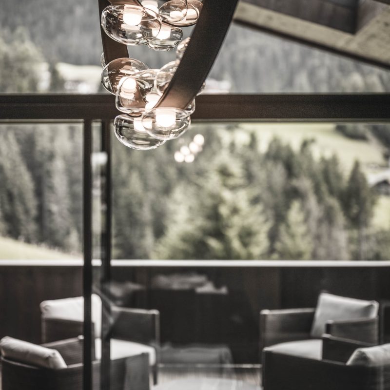 Lampadario di design e salottino sulla terrazza panoramica nella sala living all'Chalet Gardena di Cortina Hospitality, esprimendo un equilibrio sofisticato e lusso impeccabile