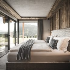 Camera matrimoniale dell'Chalet Sasslong con pareti e soffitto in legno e accesso alla terrazza panoramica.