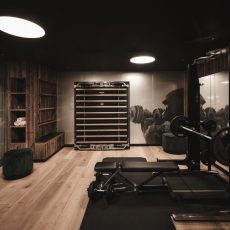 Vista della sala fitness in legno dell'Chalet Sasslong con attrezzatura completa.