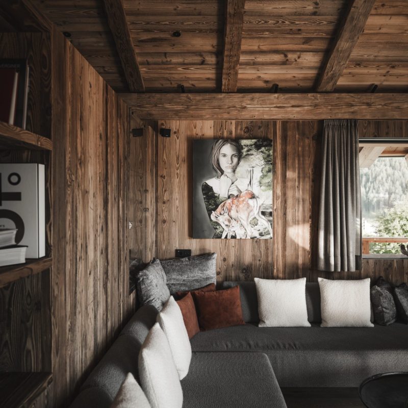 Interno del living mansardato dell'Chalet Sasslong con ampio divano e arredi in legno.
