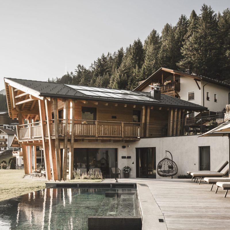 Vista esterna dell'Chalet Sasslong con piscina e solarium, circondati dallo scenario montano delle Dolomiti