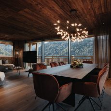 Vista della sala da pranzo in legno all'Chalet Sasslong con ampia finestra panoramica sulle Dolomiti