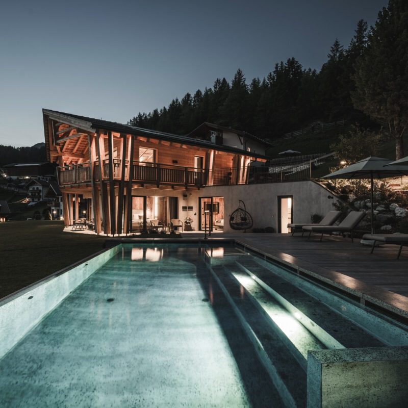 Vista notturna dell'Chalet Sasslong con piscina e solarium illuminati.